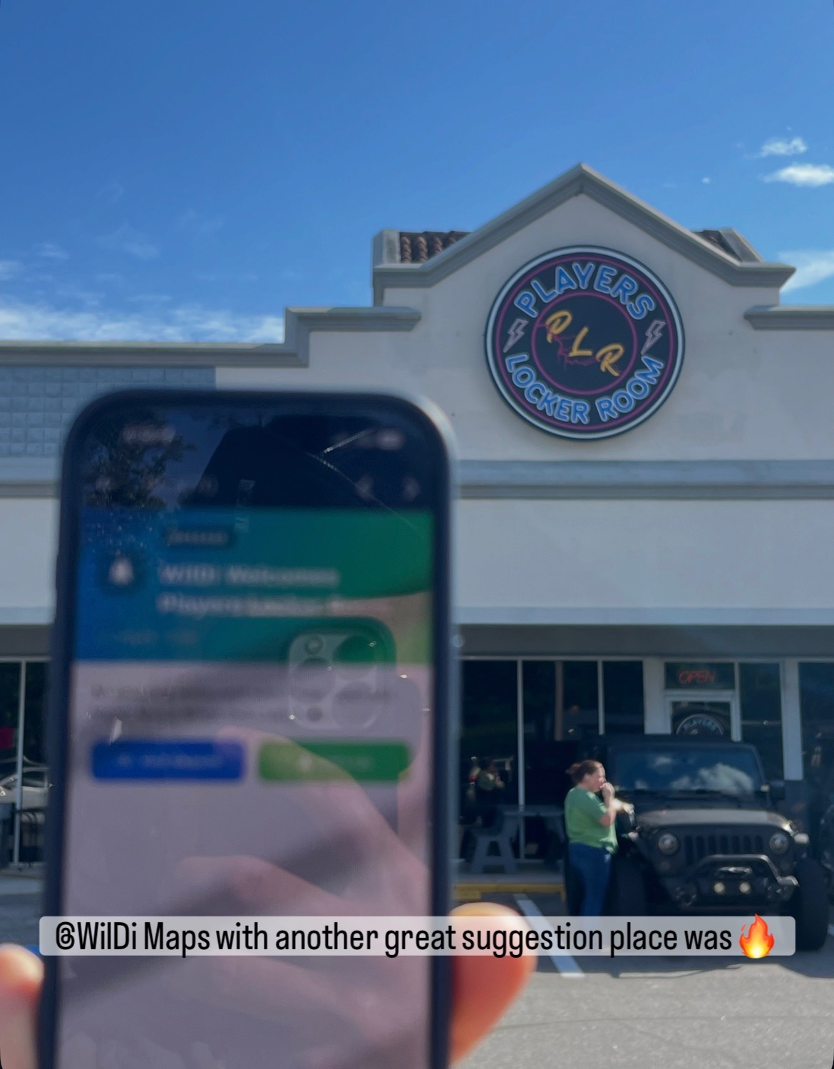 A second driver holding their phone with the WilDi notification welcoming them to Players Locker Room, standing in the parking lot in front of the neon storefront sign.